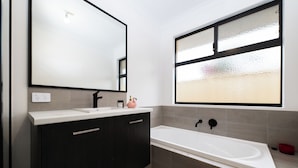 Un baño moderno con un espejo grande, una bañera y muebles oscuros.