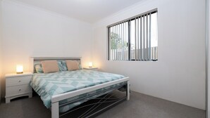 A bedroom with a bed, bedside tables, and a window with blinds.
