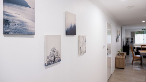 A hallway with artwork on the walls, a dining area with a table and chairs, and a view into another room.