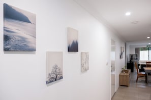 A hallway with artwork on the walls, a dining area with a table and chairs, and a view into another room. - WestPort Dwyer Premium Stay (Gosnells)