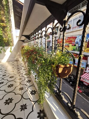 A balcony with a tiled floor, a metal railing, and hanging planters with greenery. - Localview Balcony-Trainstreet -Netflix-King Bed-Guide book (Hà Nội)