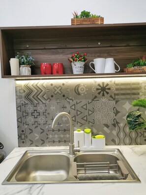 A kitchen with a stainless steel sink, a wooden shelf above it, and a patterned backsplash. - Localview Balcony-Trainstreet -Netflix-King Bed-Guide book (Hà Nội)