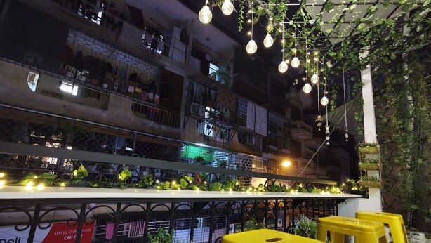 A balcony with hanging plants and lights, a railing, and a view of a building with balconies. - Localview Balcony-Trainstreet -Netflix-King Bed-Guide book (Hà Nội)