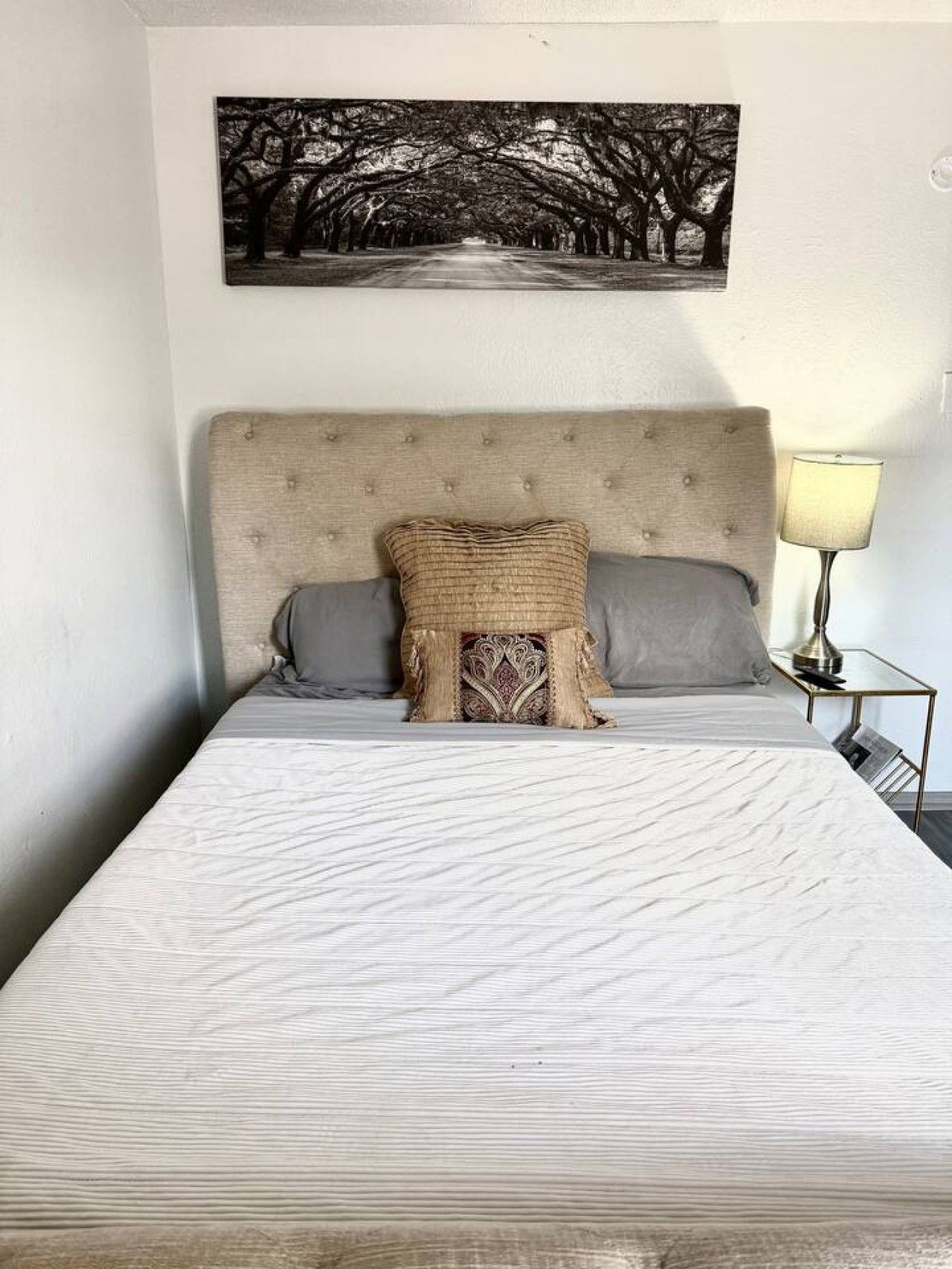 Un lit avec une tête de lit, deux oreillers, un coussin décoratif et un tableau accroché au mur.