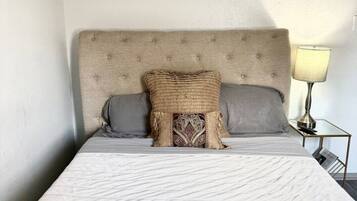 Un lit avec une tête de lit, deux oreillers, un coussin décoratif et un tableau accroché au mur.