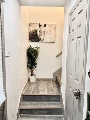 Een trap met houten details, een potplant en een kunstwerk aan de muur.