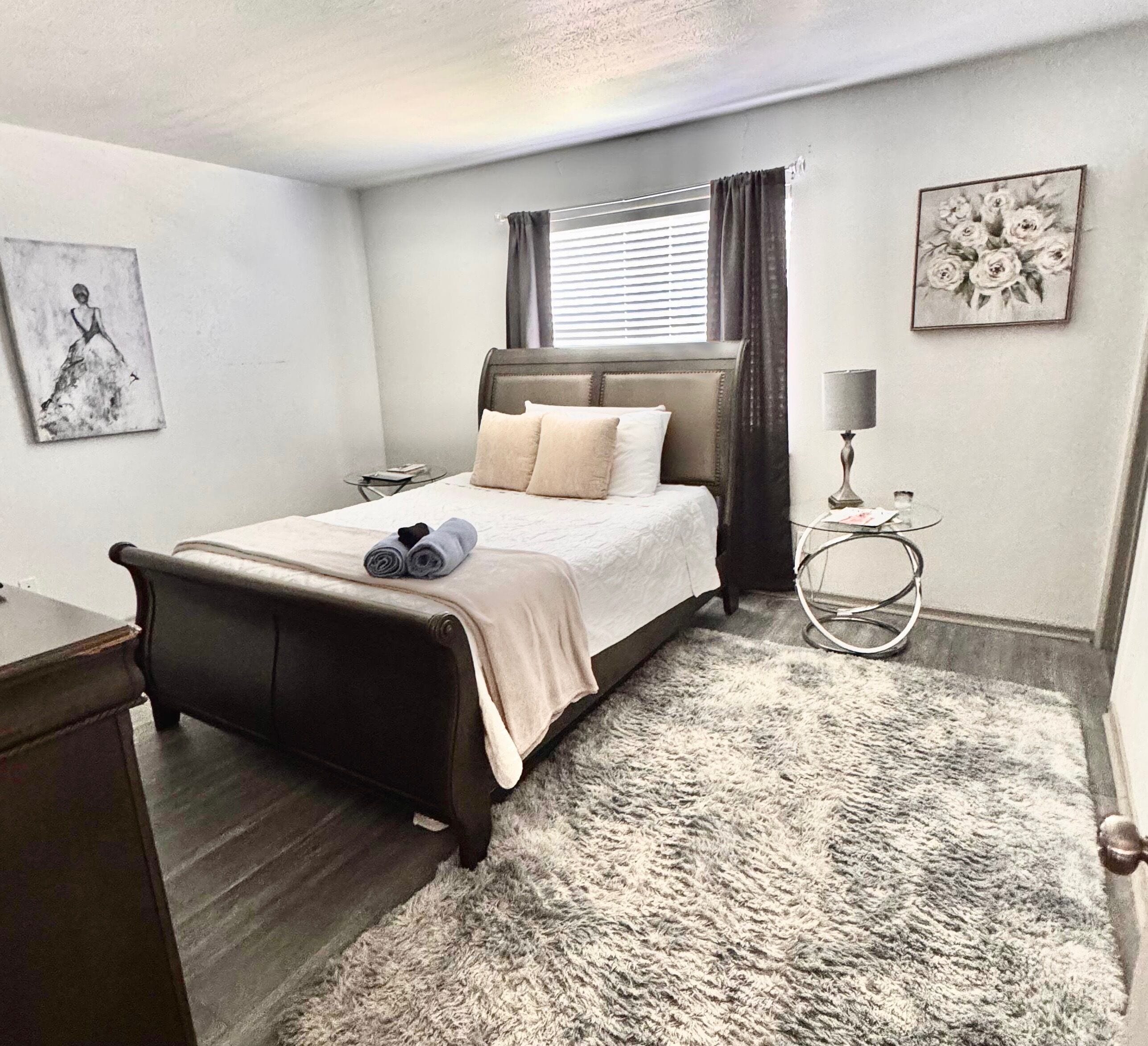 A neatly arranged bedroom with a bed, bedside tables, a lamp, and artwork on the walls.