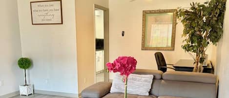 A modern living room with a grey sofa, a round coffee table with a vase of flowers, and a ceiling fan.