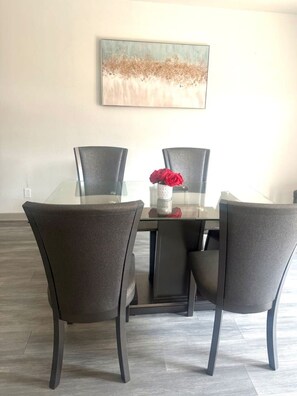 Een eetruimte met een glazen tafel, vier stoelen en een vaas met rode bloemen.