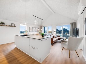 A modern kitchen with a central island, a dining area with a sofa, and large windows offering a view of the outside. - "Thormund" - 400m from the sea by Interhome (Ringkøbing)