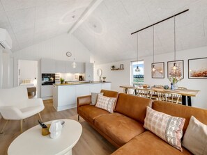 Een ruime woonkamer met een bruine leren bank, een witte salontafel, en een keuken op de achtergrond.