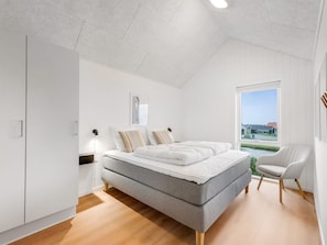A modern bedroom with a large bed, a wardrobe, a window with a view, and a chair. - "Thormund" - 400m from the sea by Interhome (Ringkøbing)