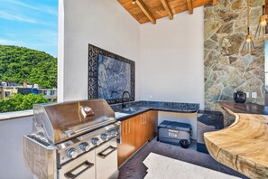 An outdoor kitchen with a stainless steel grill, wooden cabinets, and a stone wall. - Family-Friendly Apartment in Puerto Vallarta (Puerto Vallarta)