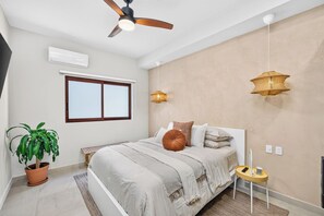 A bedroom with a bed, a ceiling fan, an air conditioner, a window, a potted plant, and a bedside table with a lamp. - Family-Friendly Apartment in Puerto Vallarta (Puerto Vallarta)