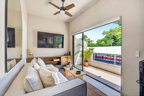 A modern living room with a sofa, a coffee table, and a television. There is a balcony with a view of the street and greenery. - Family-Friendly Apartment in Puerto Vallarta (Puerto Vallarta)