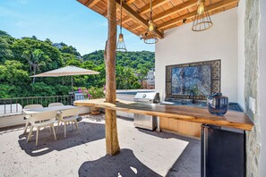 An outdoor patio with a wooden table, chairs, a grill, and a view of a lush green landscape. - Family-Friendly Apartment in Puerto Vallarta (Puerto Vallarta)