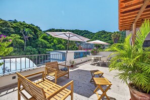A rooftop terrace with wooden furniture, umbrellas, and a view of a lush green hillside. - Family-Friendly Apartment in Puerto Vallarta (Puerto Vallarta)
