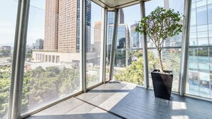 Ein modernes Interieur mit großen Fenstern, einer Zimmerpflanze und Blick auf Stadtgebäude.