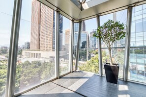 Ein modernes Interieur mit großen Fenstern, einer Zimmerpflanze und Blick auf Stadtgebäude.