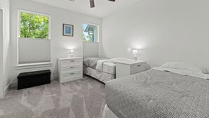 Une chambre à coucher comprenant un lit, deux tables de chevet, un ventilateur de plafond et deux fenêtres équipées de stores.