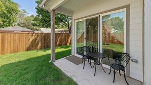 Une terrasse couverte avec une table et des chaises, une porte-fenêtre coulissante et une clôture en bois en arrière-plan.