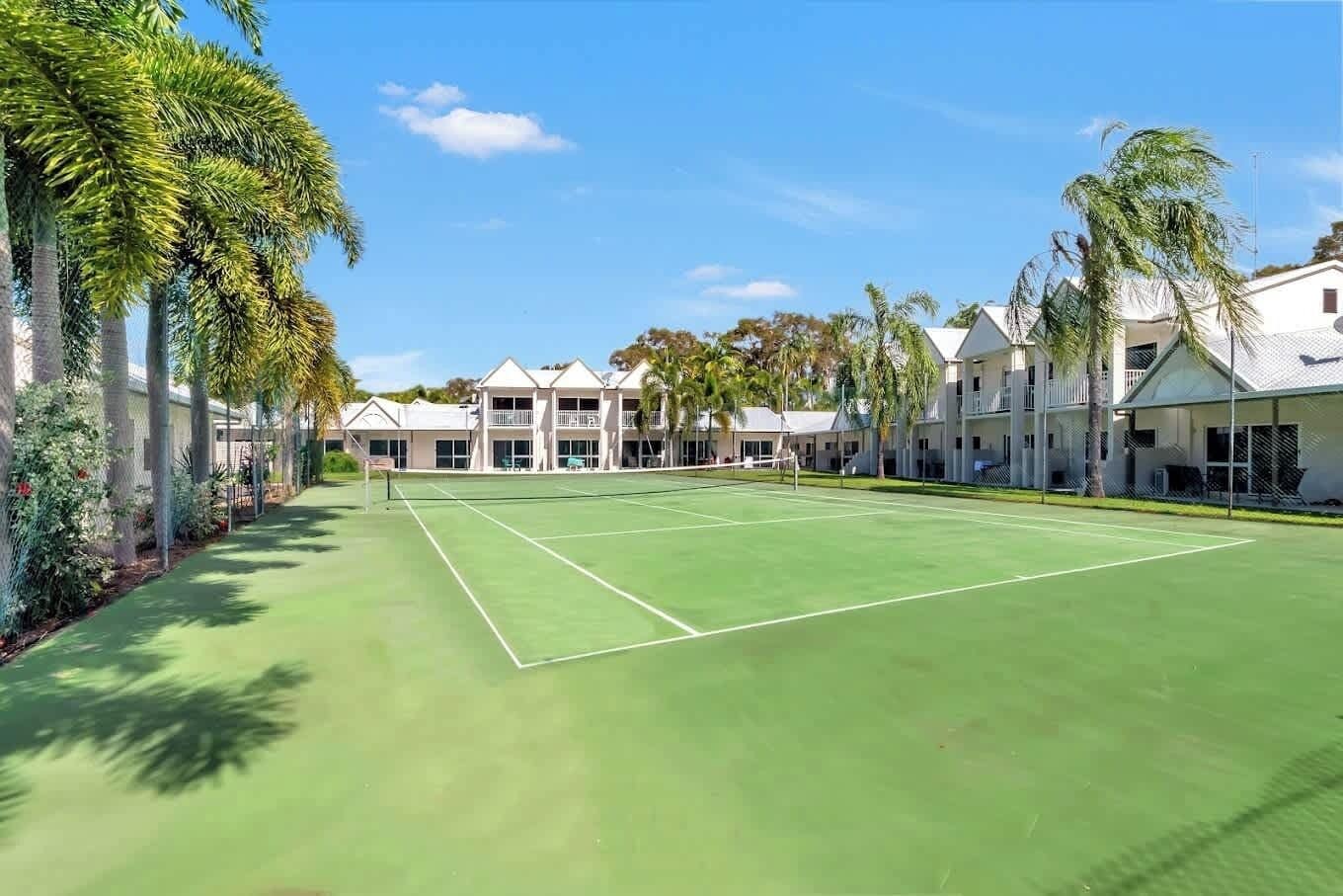 Ein Tennisplatz mit Netz, umgeben von Palmen und einer Reihe weißer Gebäude mit Balkonen.