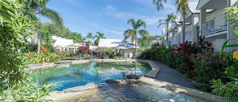 Un área de piscina en un complejo turístico con un manantial termal, rodeada de exuberante vegetación y palmeras.