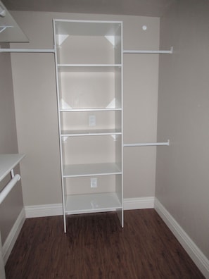 Un dressing avec des étagères blanches, une tringle à vêtements et un plancher en bois.