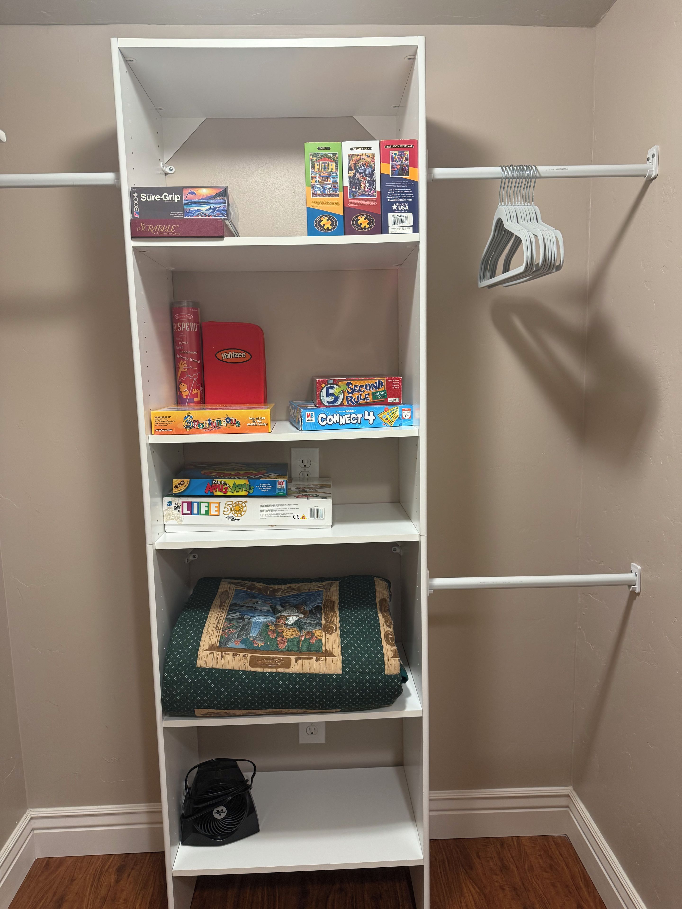 A white bookshelf with various board games and a quilt.