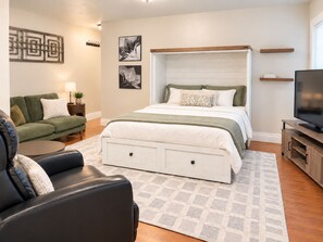Ein modernes Schlafzimmer mit einem großen Bett, einer Sitzecke, einem Fernseher und Kunstwerken an den Wänden.