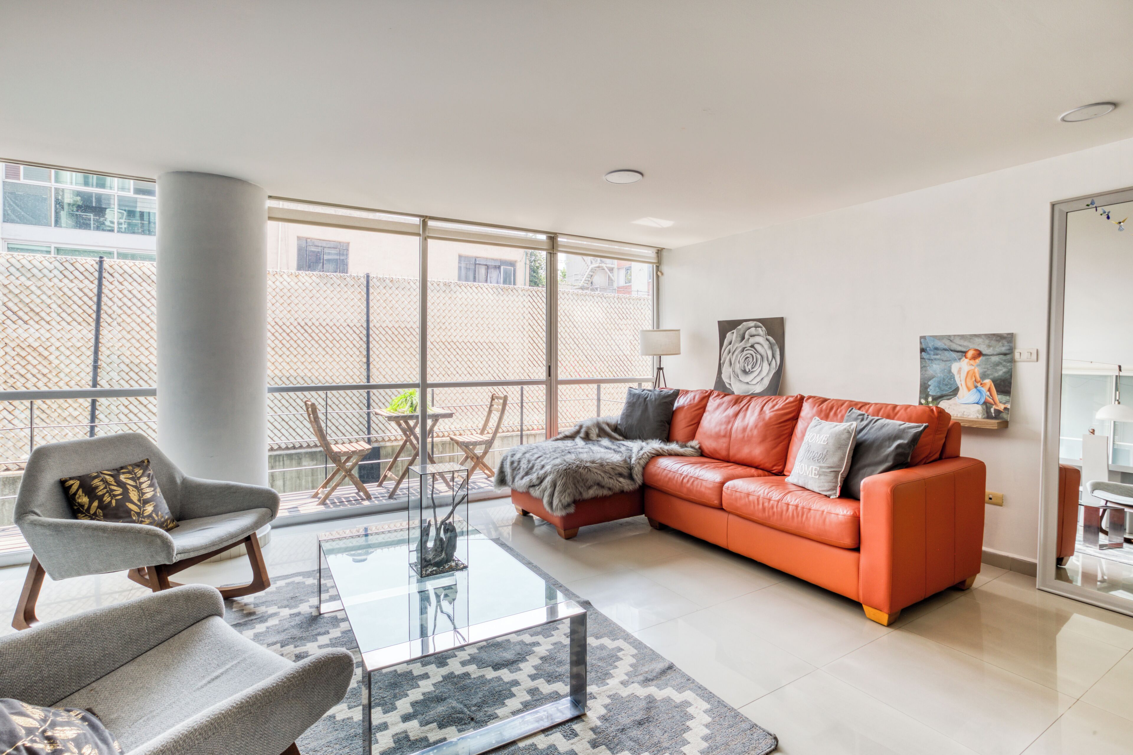 Una sala moderna con un sofá de cuero, una mesa de centro de vidrio y un sillón gris. Hay un balcón con vistas a la ciudad.