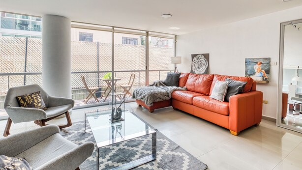 A modern living room with a leather sofa, a glass coffee table, and a grey armchair. There is a balcony with a view of the city. - Reforma Elegance · A Pasos del Ángel (Ciudad de México)