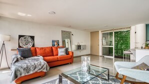 A modern living room with a glass coffee table, orange sofa, and a view of a green outdoor area. - Reforma Elegance · A Pasos del Ángel (Ciudad de México)