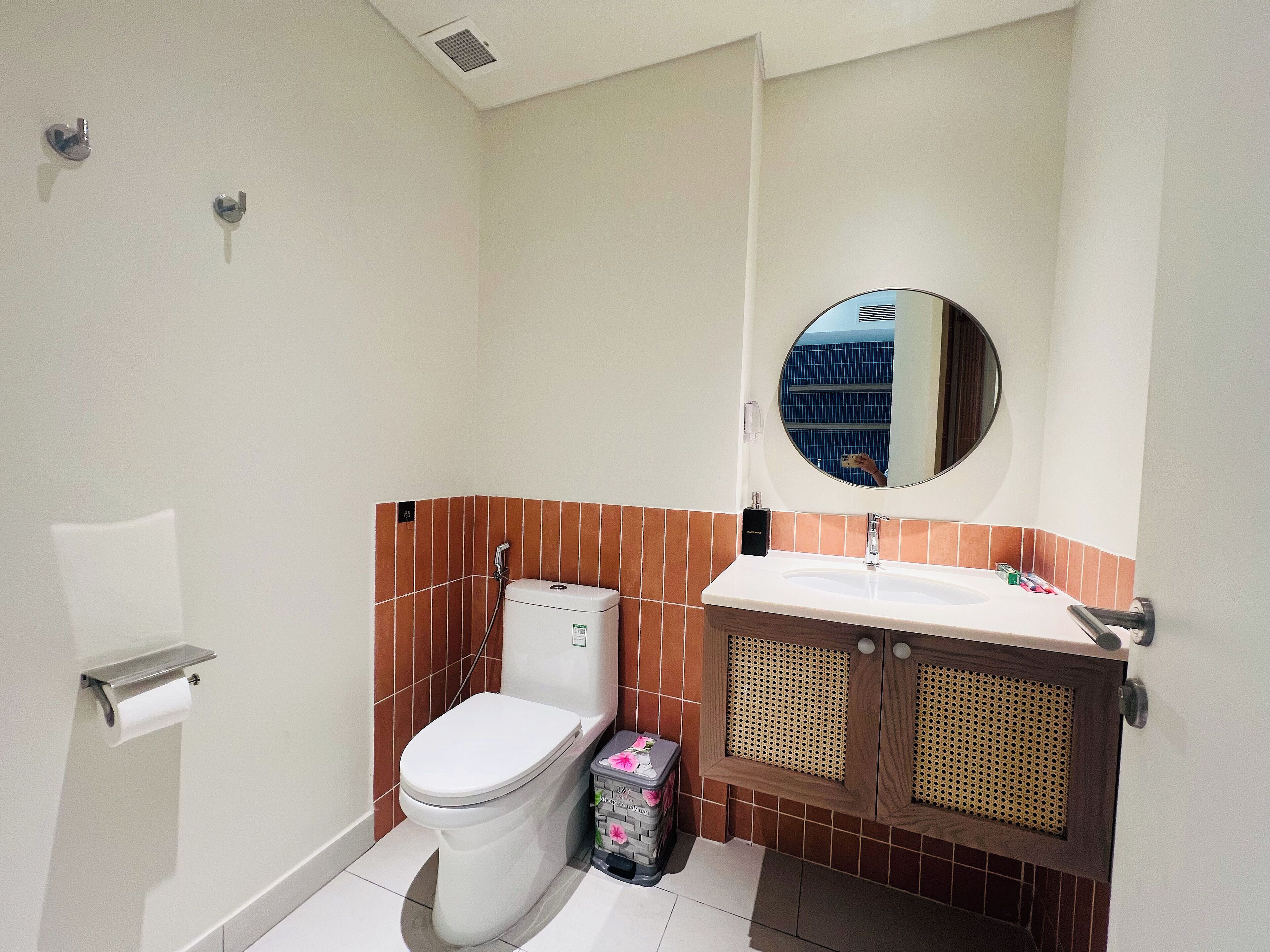 A bathroom with a toilet, sink, mirror, and a trash bin.