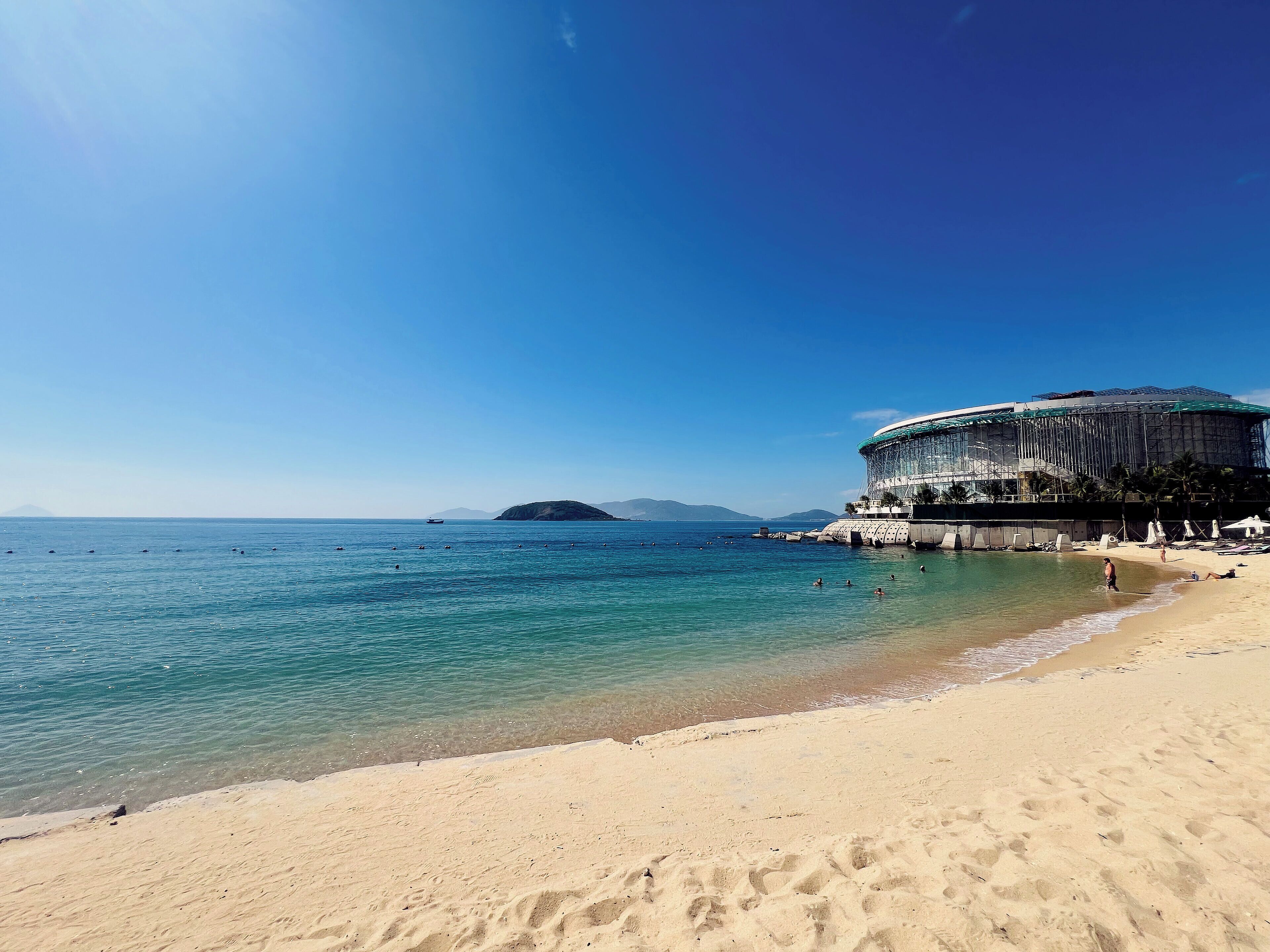 A beach with clear water, a sandy shore, and a large building with a unique design.