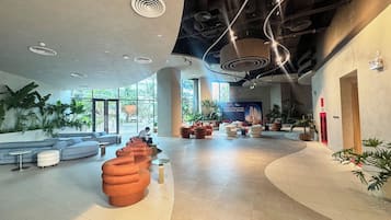 Un hallo amplio con una zona de estar curvada, un cartel grande y una combinación de iluminación natural y artificial.