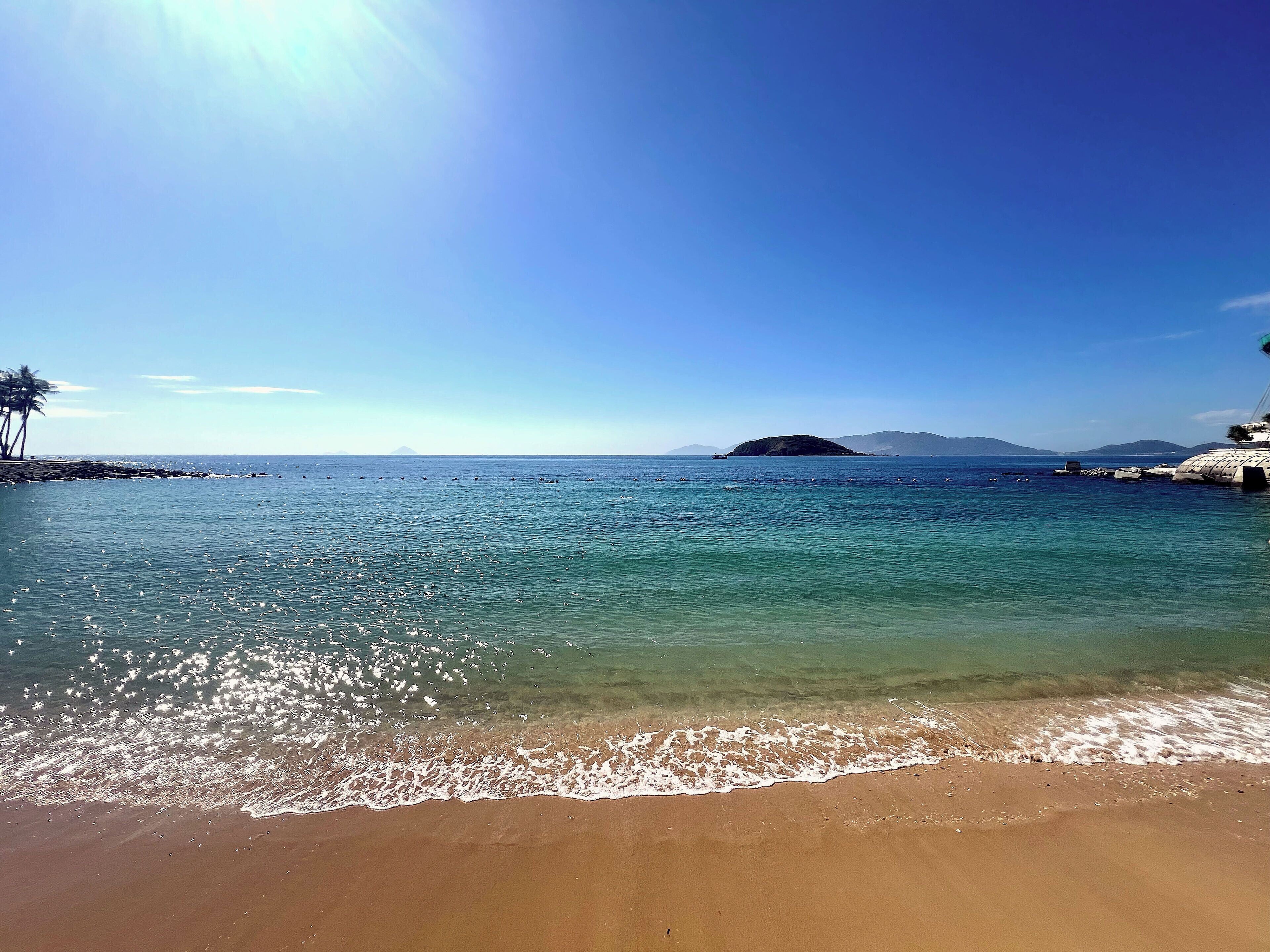 A beach with clear water, a sandy shore, and a distant island.