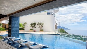 A modern pool area with lounge chairs, a clear view of the sea, and a white building with a balcony. - Bai Tien Ocean Front Residences (Bac Nha Trang)