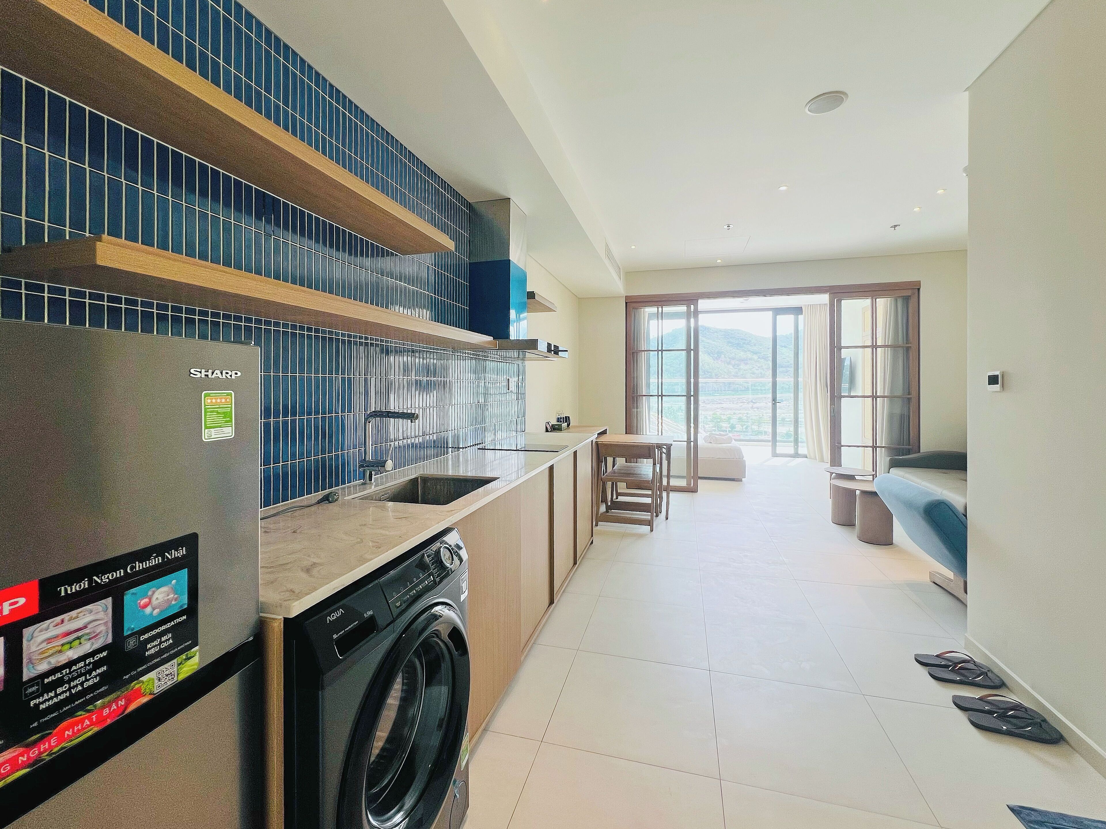 A modern kitchen with a Sharp refrigerator, an Aquia washing machine, and a dining area with a view.