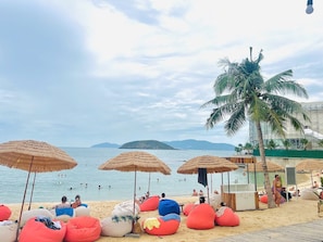 A beach with thatched umbrellas, bean bags, and a palm tree.