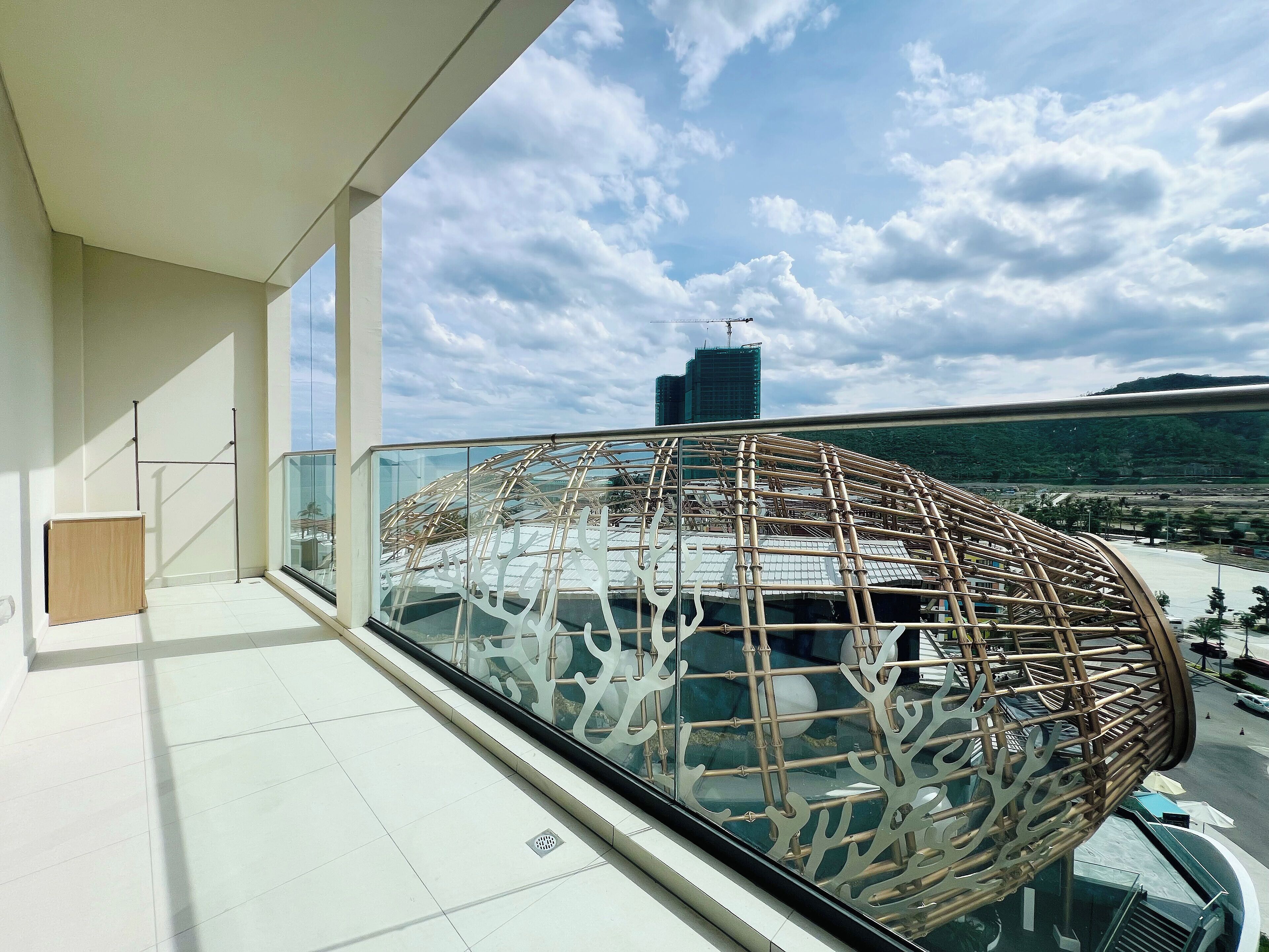 A balcony with a glass railing, a view of a cityscape, and a bamboo structure.