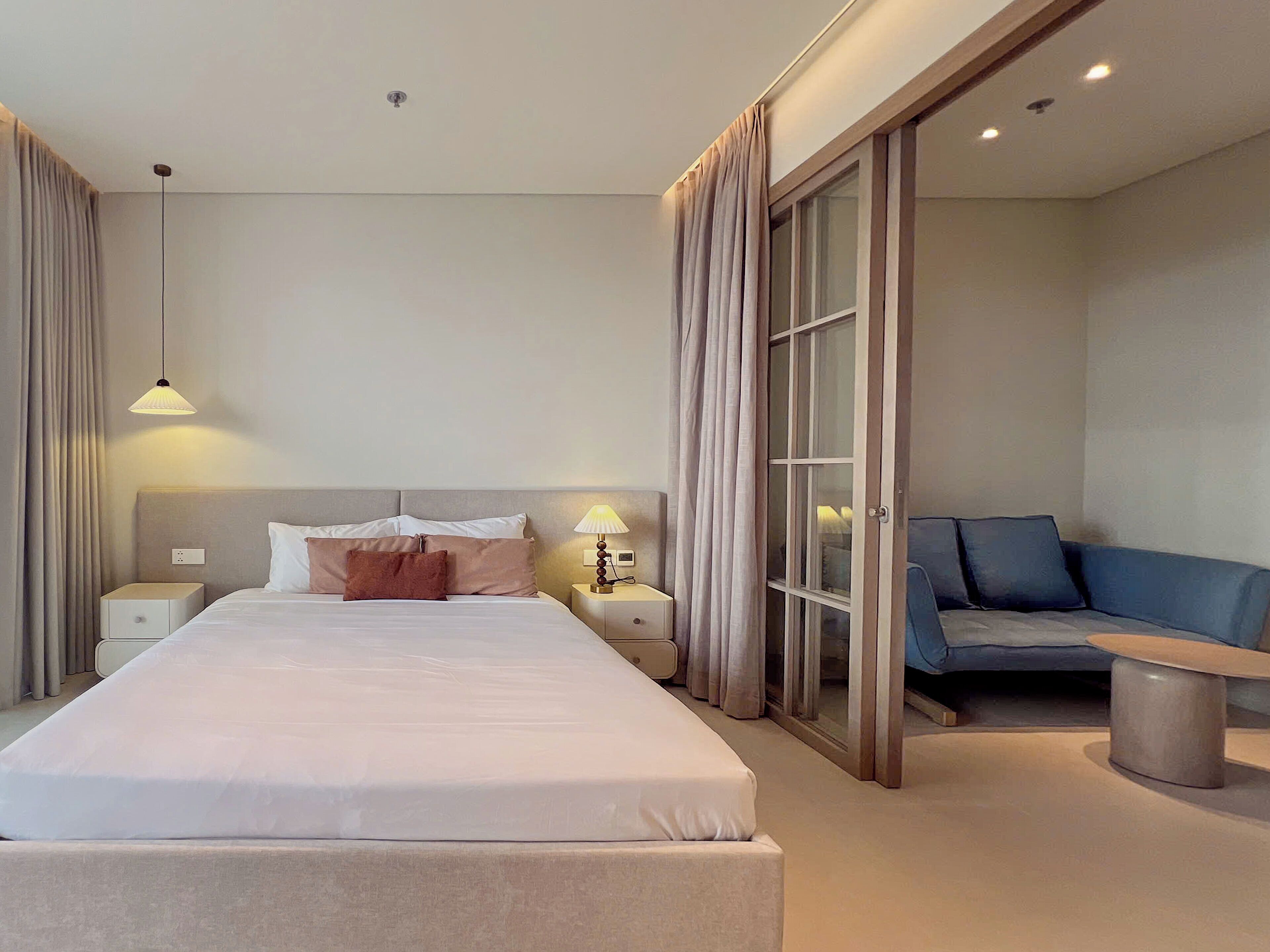 A hotel room with a large bed, bedside tables, a desk, a chair, and a sliding glass door leading to a balcony.