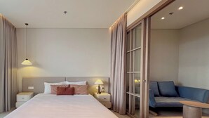 Habitación de hotel con una cama grande, mesitas de noche, un escritorio, una silla y una puerta corrediza de vidrio que da a un balcón.