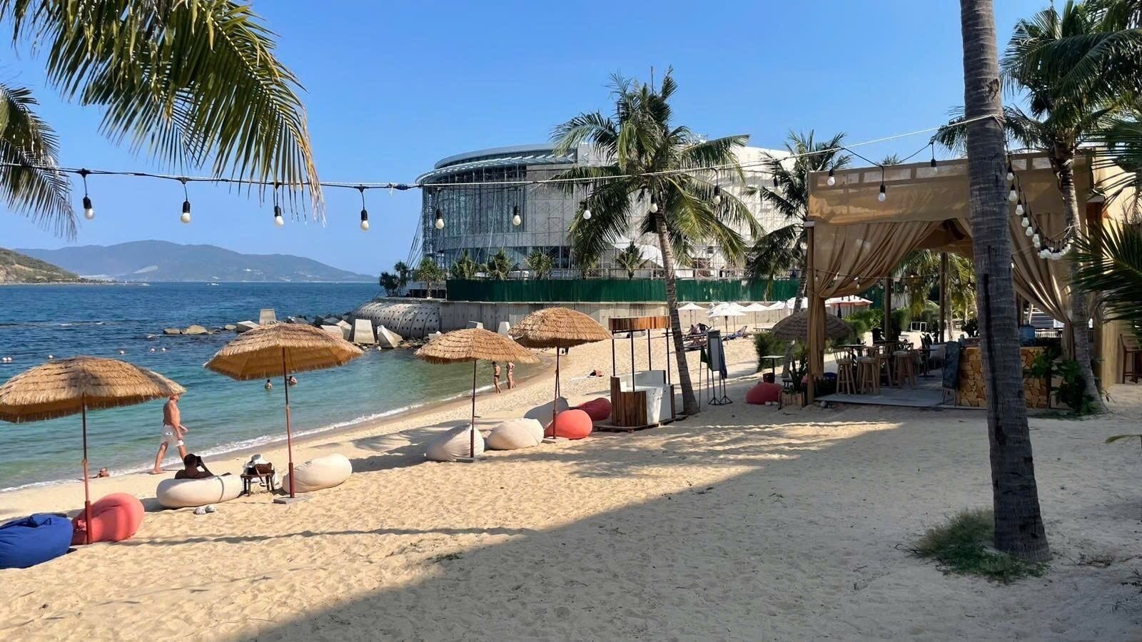 Une plage avec des parasols, des chaises longues et un bâtiment en arrière-plan.