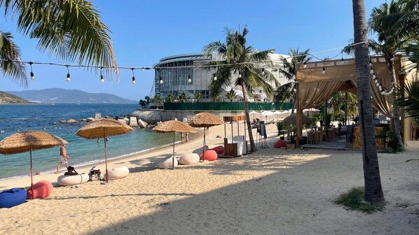 Una playa con sombrillas, sillas de descanso y un edificio al fondo.