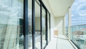 A modern balcony with glass doors, a bed, and a view of the cityscape. - Bai Tien Ocean Front Residences (Bac Nha Trang)