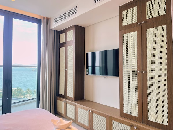 Un dormitorio con un ventanal grande, una cama, un televisor y un armario de madera con diseño tejido.