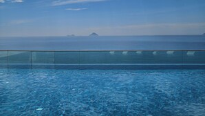 Un cielo azul despejado con nubes, un mar tranquilo y una piscina con barrera de vidrio.