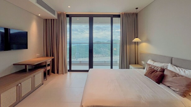 Habitación de hotel moderna con una cama grande, un televisor de pantalla plana, un escritorio y vistas a la ciudad a través del ventanal.