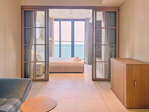 Una habitación con cama, sofá, una mesita y armario. Cuenta con un ventanal con cortinas y vistas al mar.